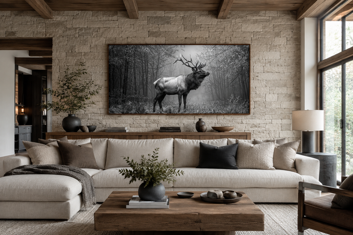 Black and white framed canvas wall art of an elk stag standing in a misty forest above a sofa.