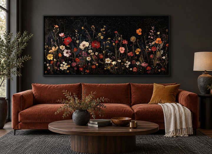 Framed canvas wall art of colorful wildflowers on a black background above a rust-colored sofa.