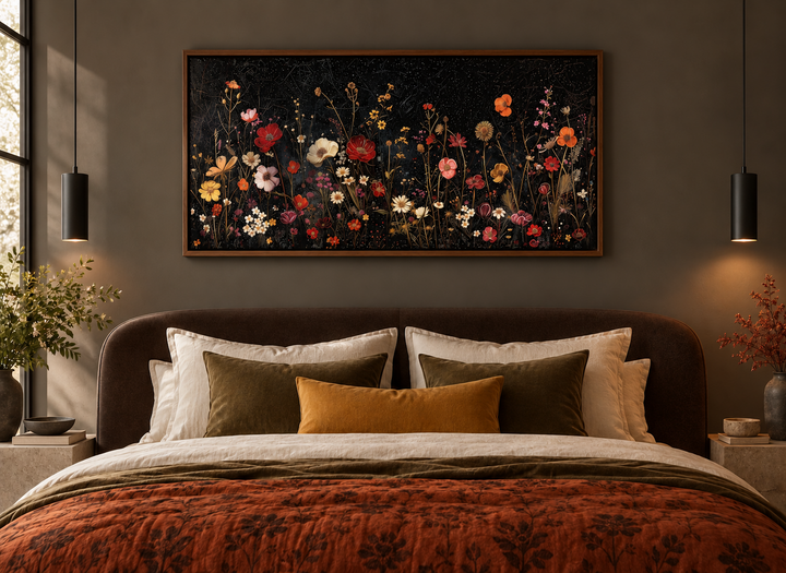 Framed canvas wall art of colorful wildflowers on a black background above a bed in a moody bedroom.