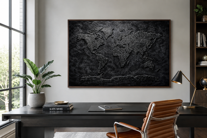 Black textured world map framed canvas wall art hanging above a dark wood desk in a modern office.