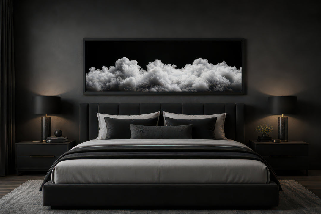 Long horizontal framed canvas wall art of black and white clouds above a bed in a dark bedroom.
