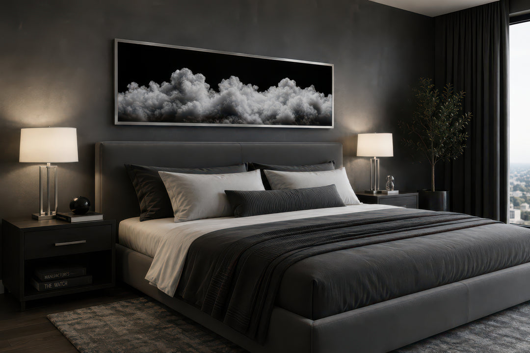 Long horizontal framed canvas wall art of black and white clouds above a bed in a modern bedroom.