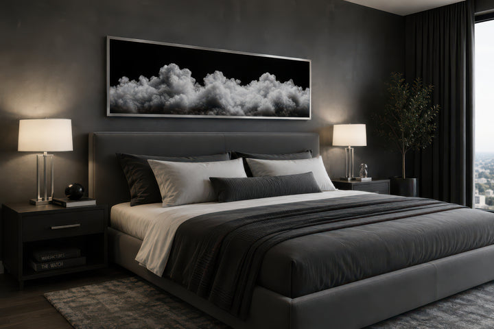 Long horizontal framed canvas wall art of black and white clouds above a bed in a modern bedroom.