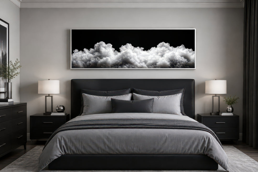 Long horizontal framed canvas wall art of black and white clouds above a modern bed.