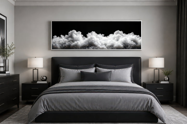 Long horizontal framed canvas wall art of black and white clouds above a modern bed.