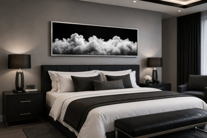 Long horizontal framed canvas wall art of black and white clouds hanging above a bed.