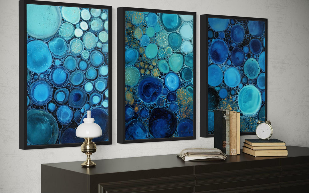 Set of 3 blue aqua and navy bubble abstract canvas prints displayed above a dark wood console table.