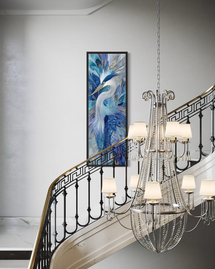 Vertical canvas print of an elegant blue heron in a black frame on a wall by a staircase.