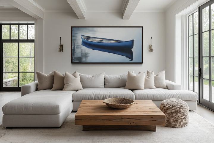 Framed canvas wall art of a blue canoe on a calm lake, hanging above a modern living room sofa.