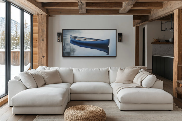 Framed canvas wall art of a blue canoe on a calm lake, hanging above a white sectional sofa.
