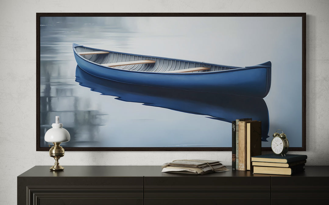 Framed canvas wall art of a blue canoe on a calm lake, displayed above a dark wooden sideboard.