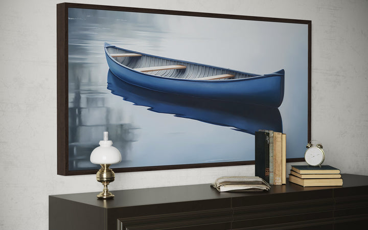 Framed canvas wall art of a blue canoe on a calm lake, displayed above a dark wood dresser.