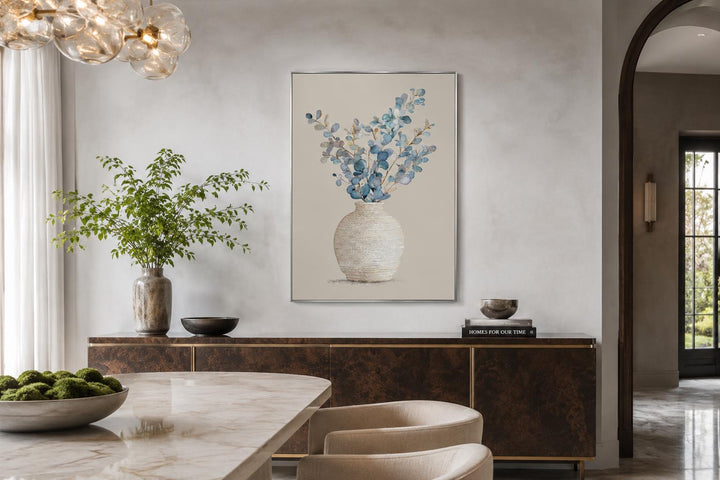 Blue floral still life wall art with eucalyptus branches in a textured vase over a dining sideboard.