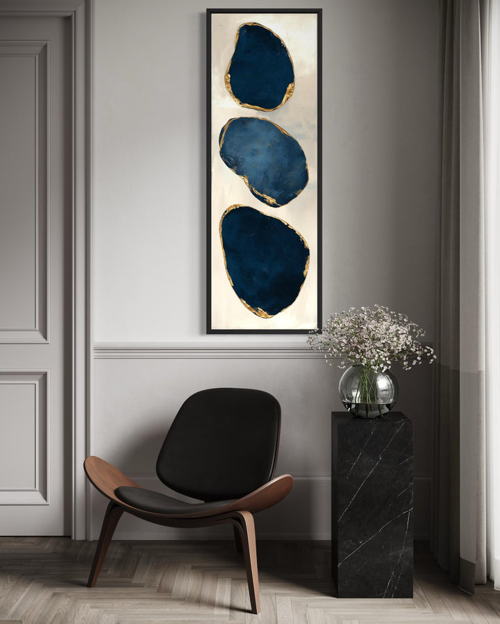 Vertical narrow canvas print featuring three abstract blue stones with gold edges in a black frame.