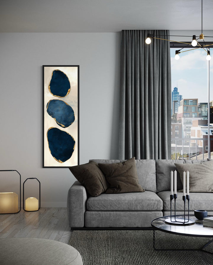 Vertical narrow canvas print featuring three abstract blue stones with gold edges on a light wall.