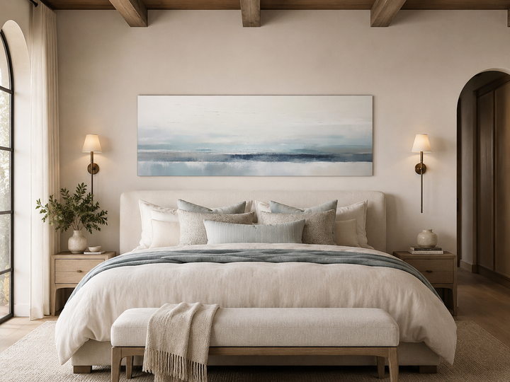 Long horizontal blue and gray abstract coastal canvas wall art hanging above a bed.