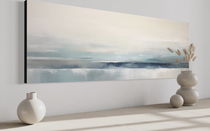 Blue gray calm coastal abstract framed canvas wall art displayed above a shelf with vases.