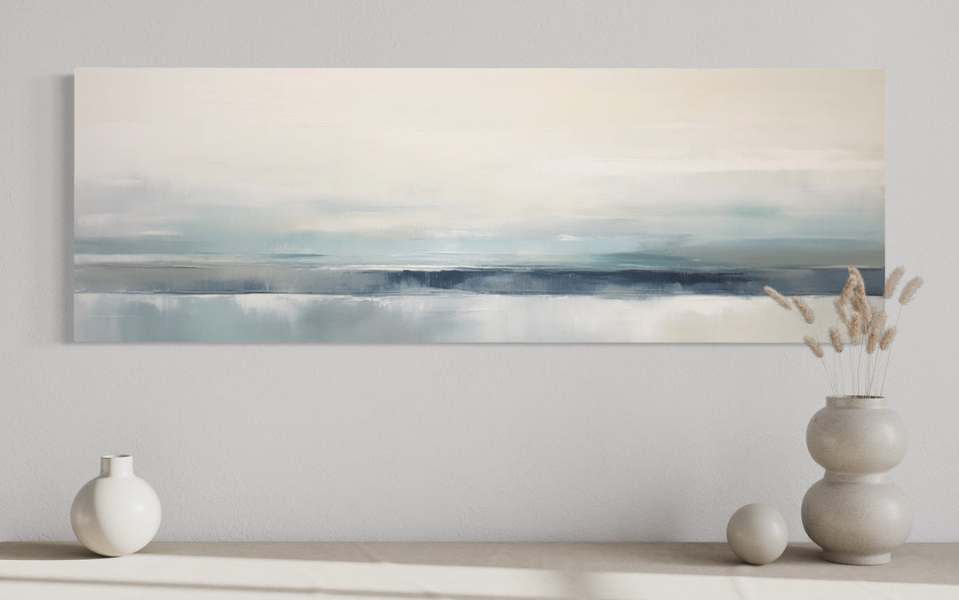 Blue gray calm coastal abstract landscape framed canvas wall art displayed over a console table.