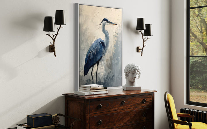 Vertical framed canvas wall art featuring an abstract blue heron painting above a wooden dresser.