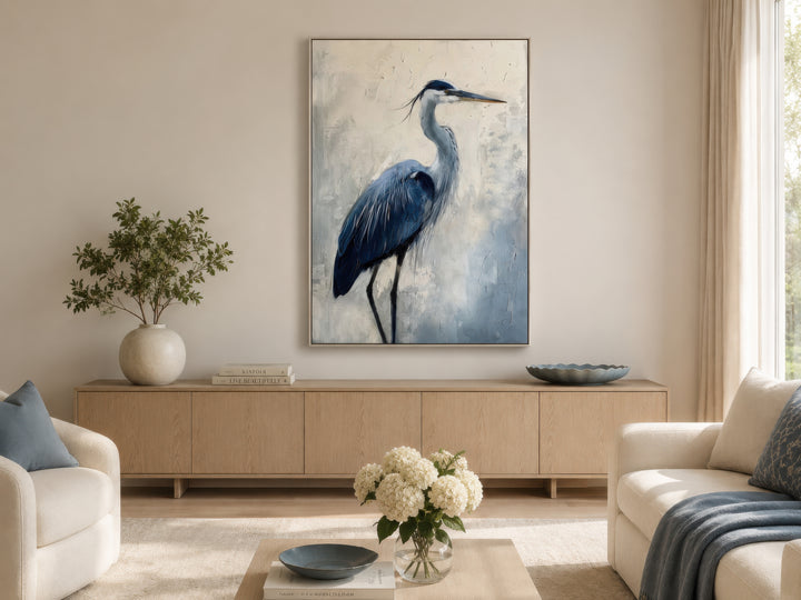 Blue heron abstract painting in a thin silver frame hanging above a light wood sideboard.