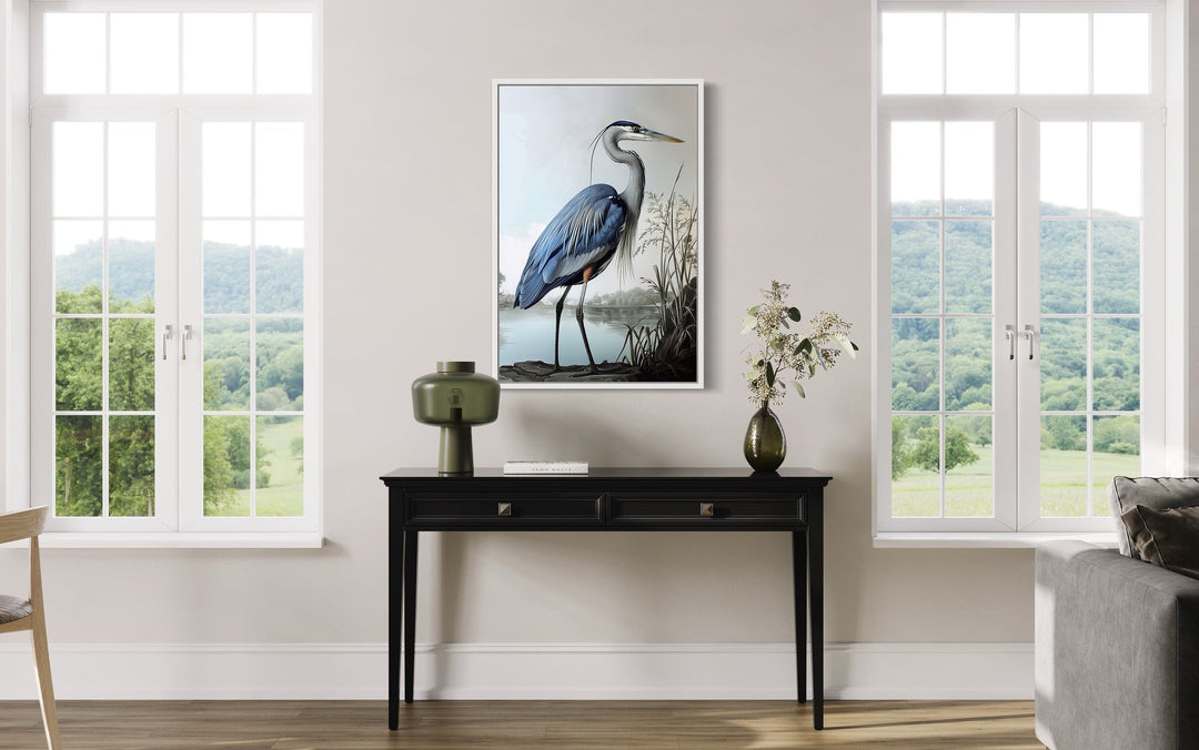 Framed canvas wall art of a blue heron on a shoreline, displayed above a black console table.