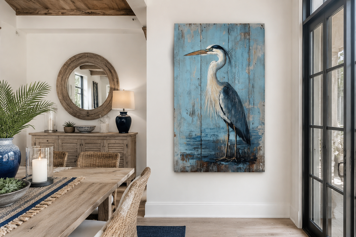 Rustic blue heron painting on a weathered wood-textured vertical canvas in a coastal dining room.