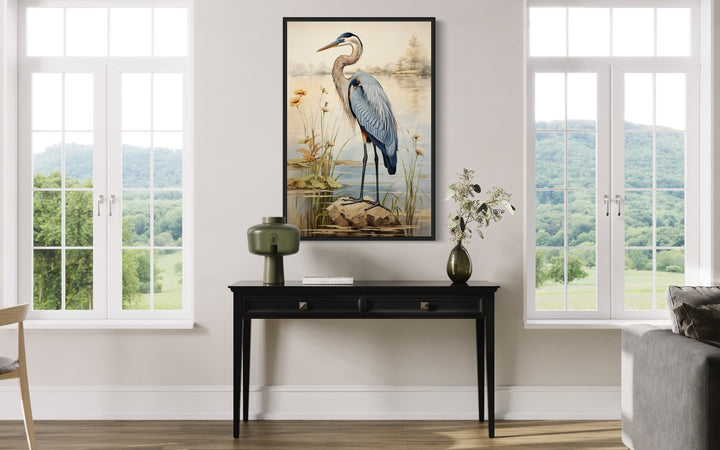Vintage blue heron framed canvas wall art hanging above a black console table in a bright room.