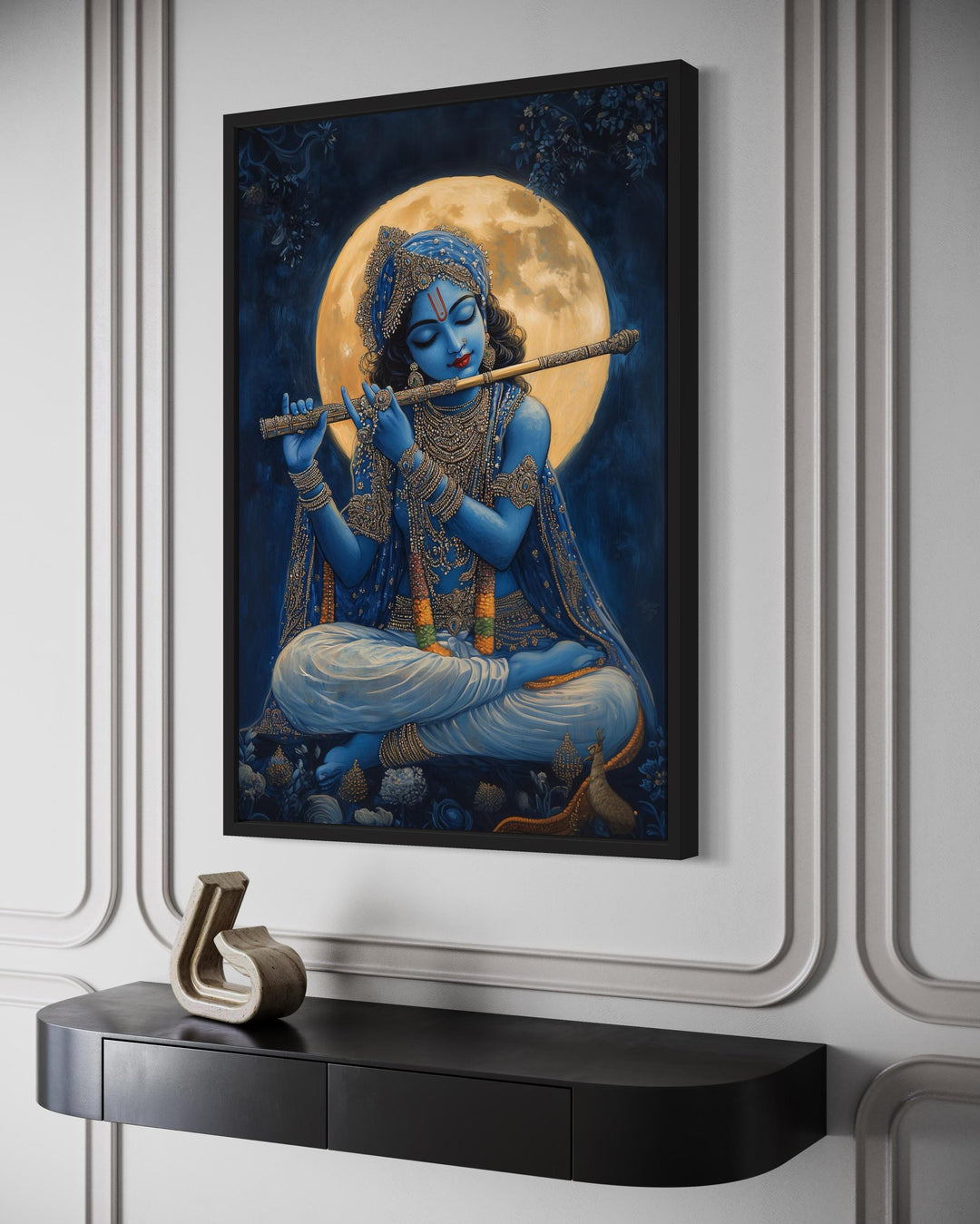 Blue Krishna playing flute under a full moon framed canvas wall art above a black console table.