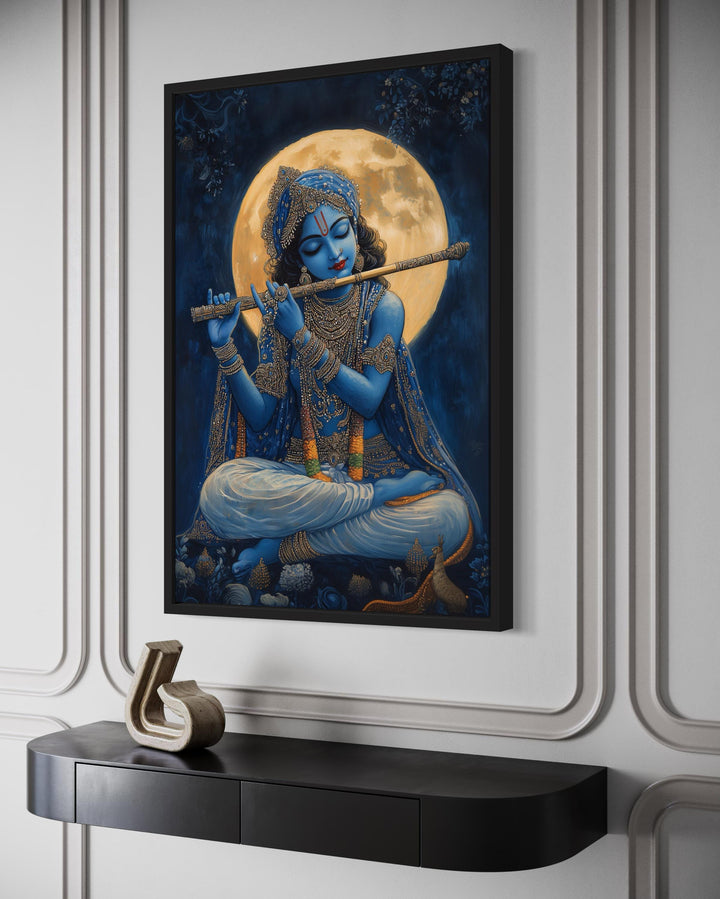 Blue Krishna playing flute under a full moon framed canvas wall art above a black console table.