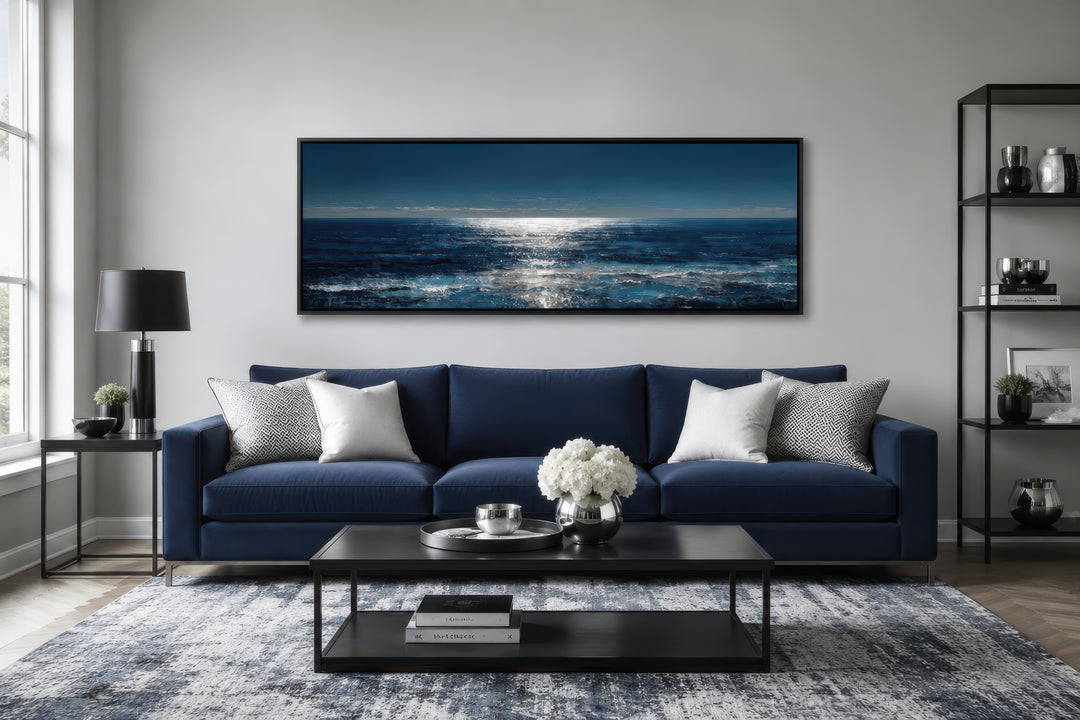 A long horizontal seascape canvas featuring a moonlit blue and silver ocean over a navy sofa.