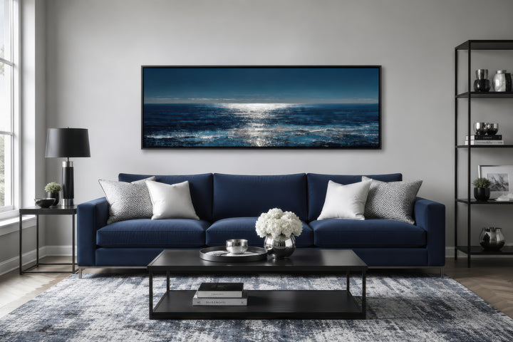 A long horizontal seascape canvas featuring a moonlit blue and silver ocean over a navy sofa.