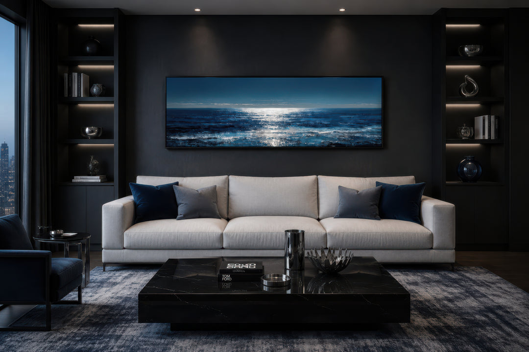 Blue and silver horizontal seascape wall art hanging above a modern white sofa in a dark room.