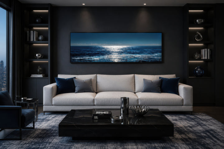 Blue and silver horizontal seascape wall art hanging above a modern white sofa in a dark room.