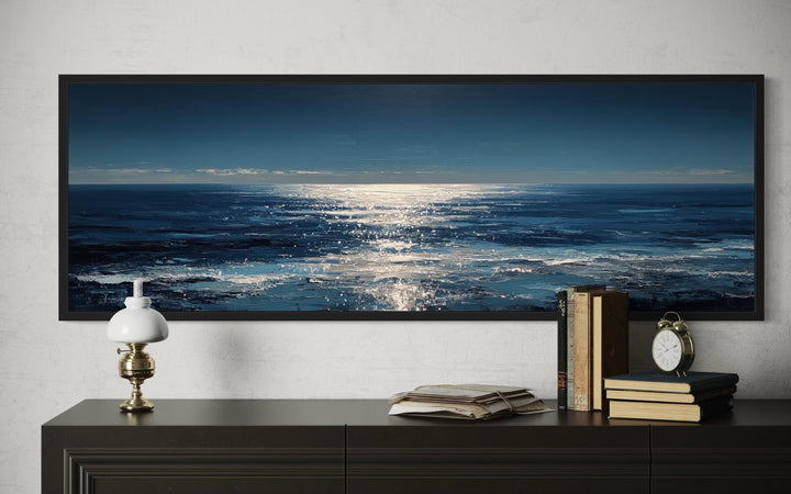 A long horizontal seascape painting of a moonlit blue ocean hangs above a dark wooden dresser.