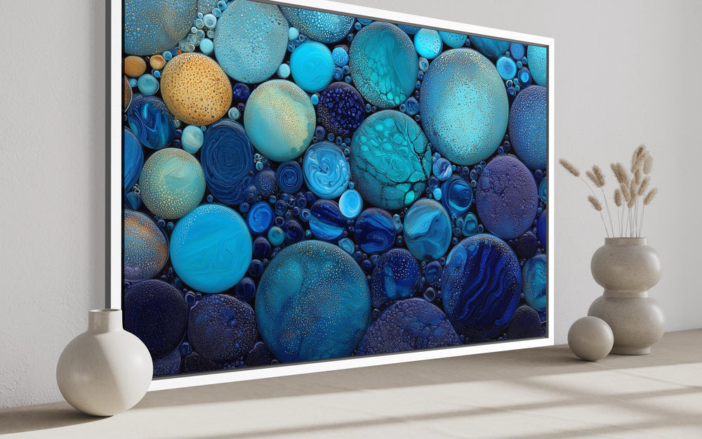 Abstract coastal canvas wall art featuring blue and teal circular rock-like forms in a white frame.