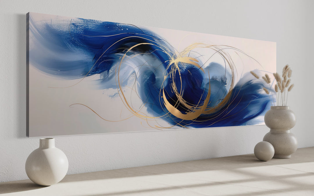 Narrow horizontal abstract wall art with blue, white, and gold brushstrokes on a white wall.