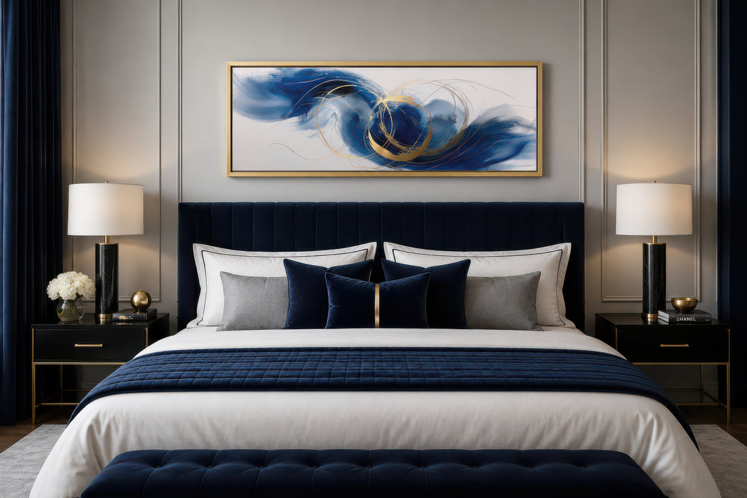 Narrow horizontal abstract wall art with blue, white, and gold swirls hanging above a navy bed.