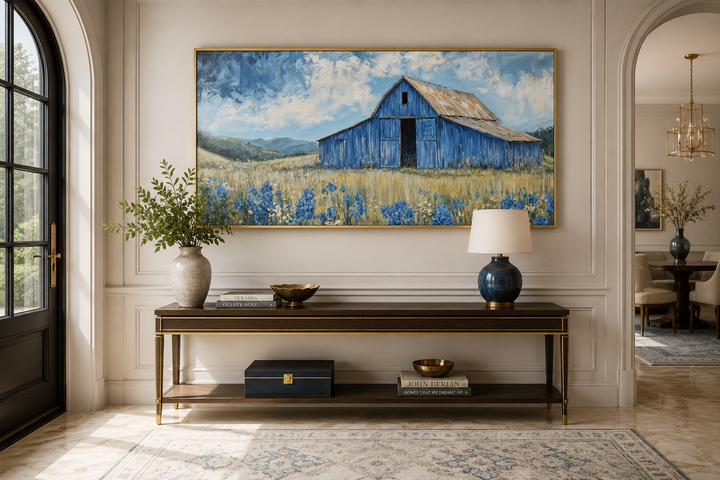 Framed canvas wall art of a rustic blue barn in a field of bluebonnets above a console table.