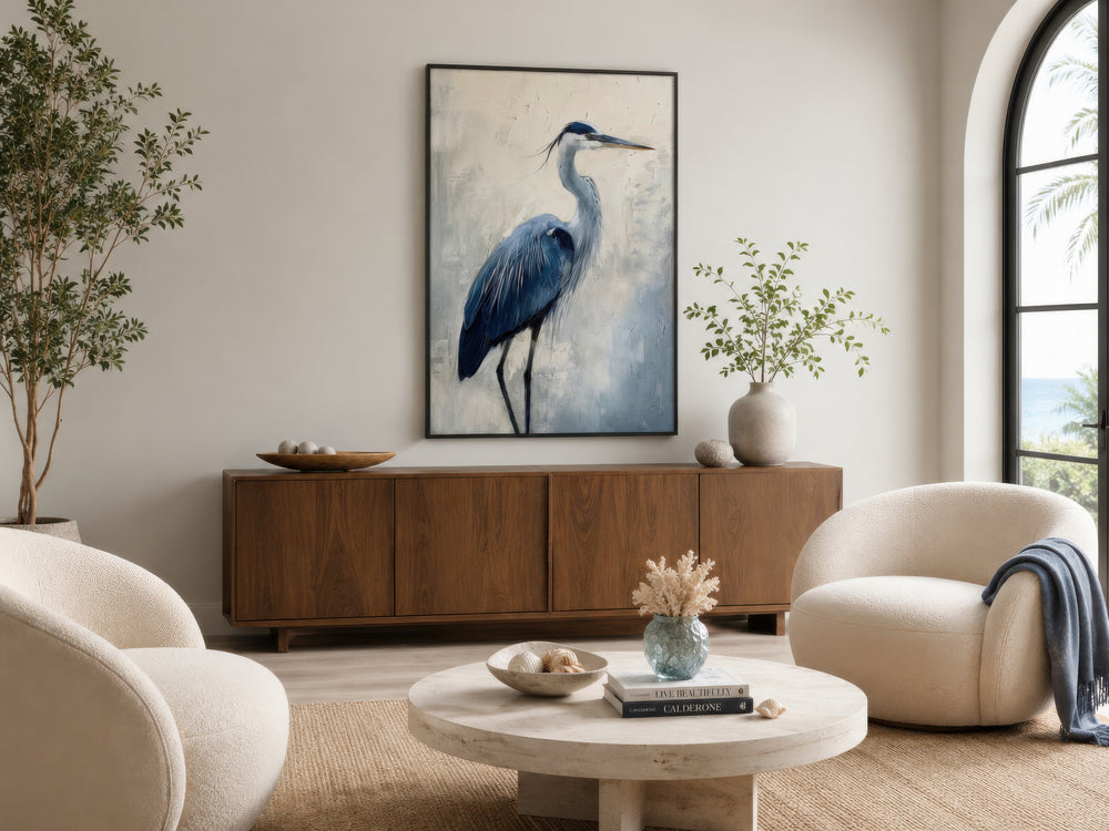 Blue heron abstract painting in a black frame, hanging above a wooden sideboard in a coastal room.