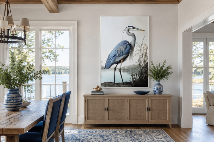 Large framed canvas wall art of a blue heron hanging above a wooden sideboard in a coastal room.