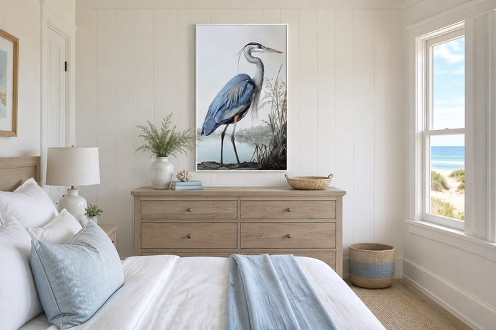 Framed canvas wall art of a majestic blue heron in a coastal setting above a wooden dresser.