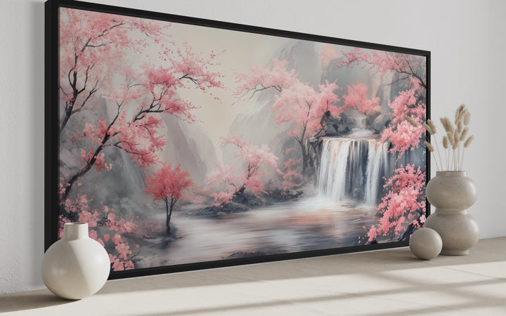 Framed canvas wall art of a grey waterfall and blush pink cherry blossoms in a serene landscape.