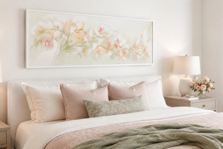 Blush pink floral watercolor canvas painting in a white frame hanging above a bed.