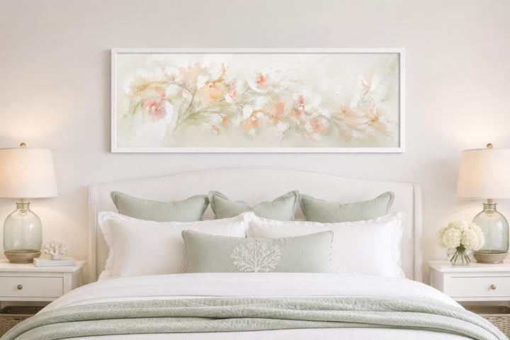 Blush pink floral watercolor canvas wall art in a long horizontal white frame above a bed.