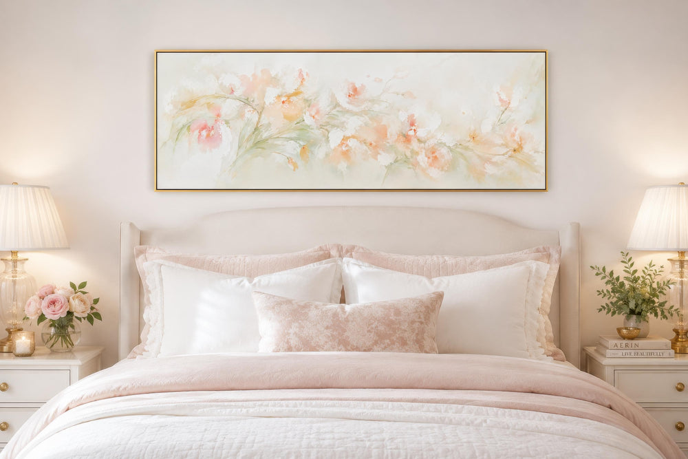 Blush pink floral watercolor canvas wall art in a gold frame above a bed with pink and white linens.