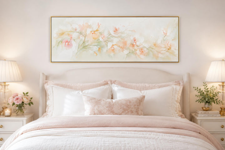Blush pink floral watercolor canvas wall art in a gold frame above a bed with pink and white linens.