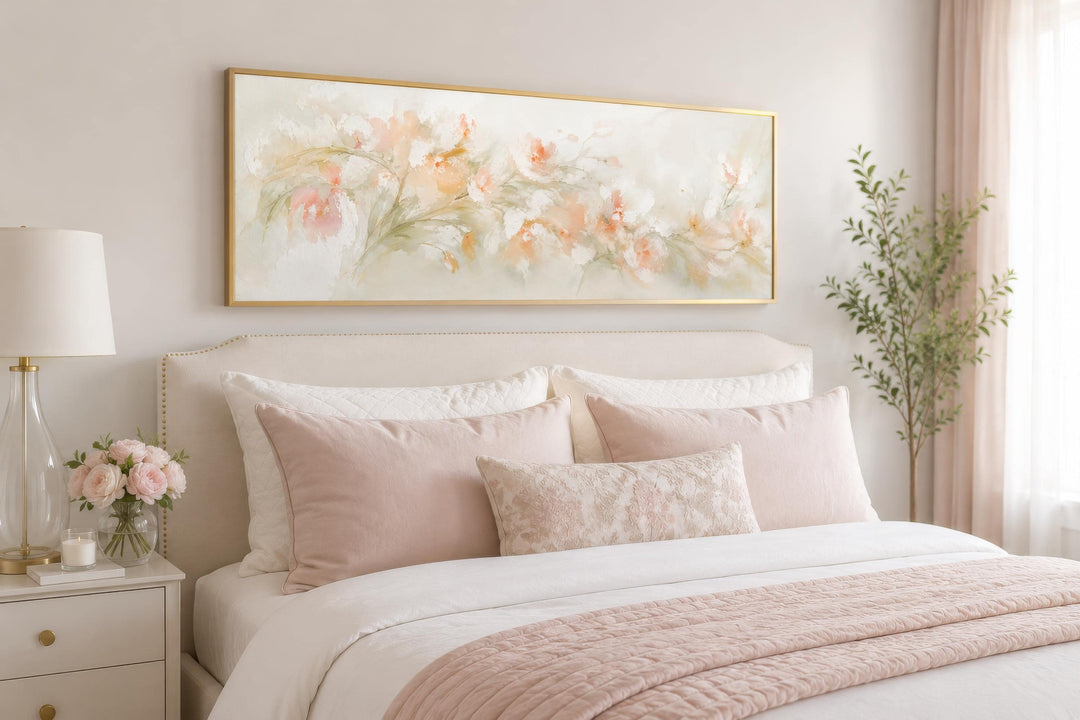 Blush pink floral watercolor canvas wall art in a gold frame hanging above a bed with pink pillows.