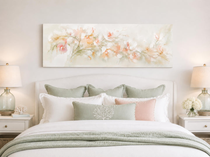 Long horizontal watercolor canvas painting of blush pink and peach flowers above a white bed.
