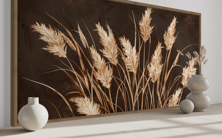 Boho framed canvas wall art featuring beige pampas grass on a dark brown textured background.