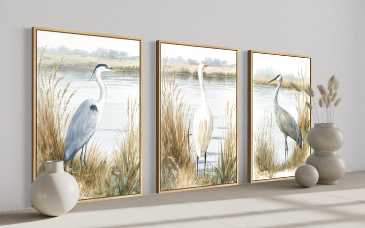 Three framed canvas prints of a heron, egret, and crane in a neutral coastal landscape.